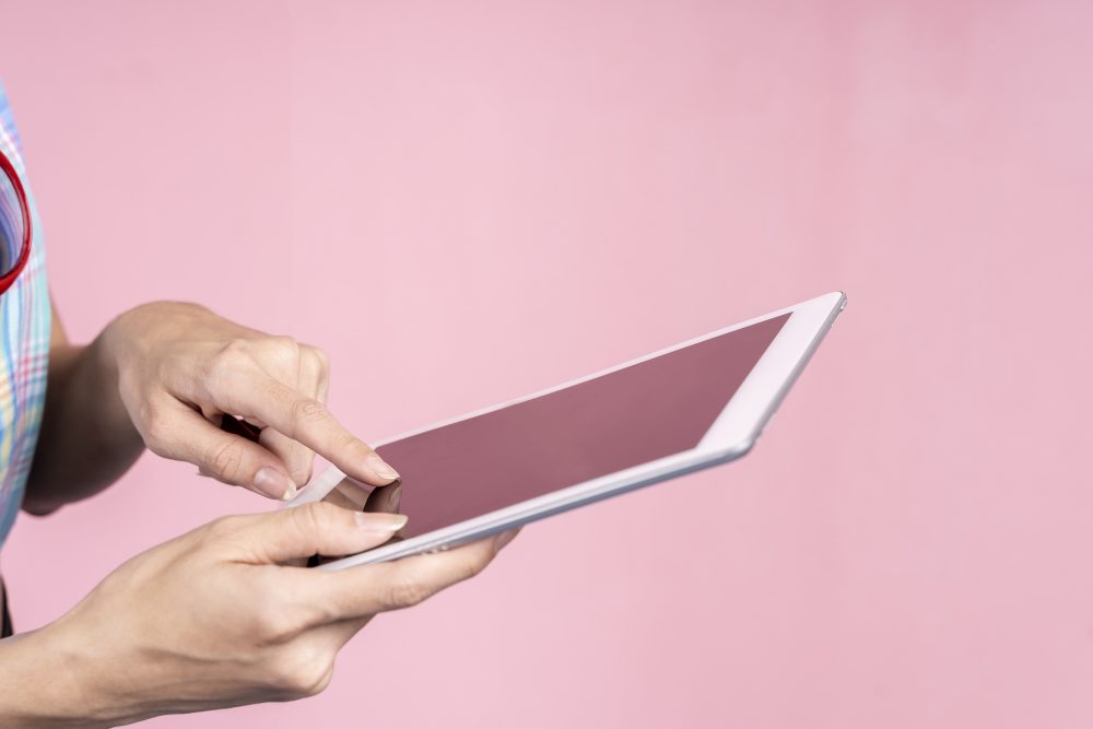 Closeup of hands using tablet with empty screen on pink background. Business and technology concept.